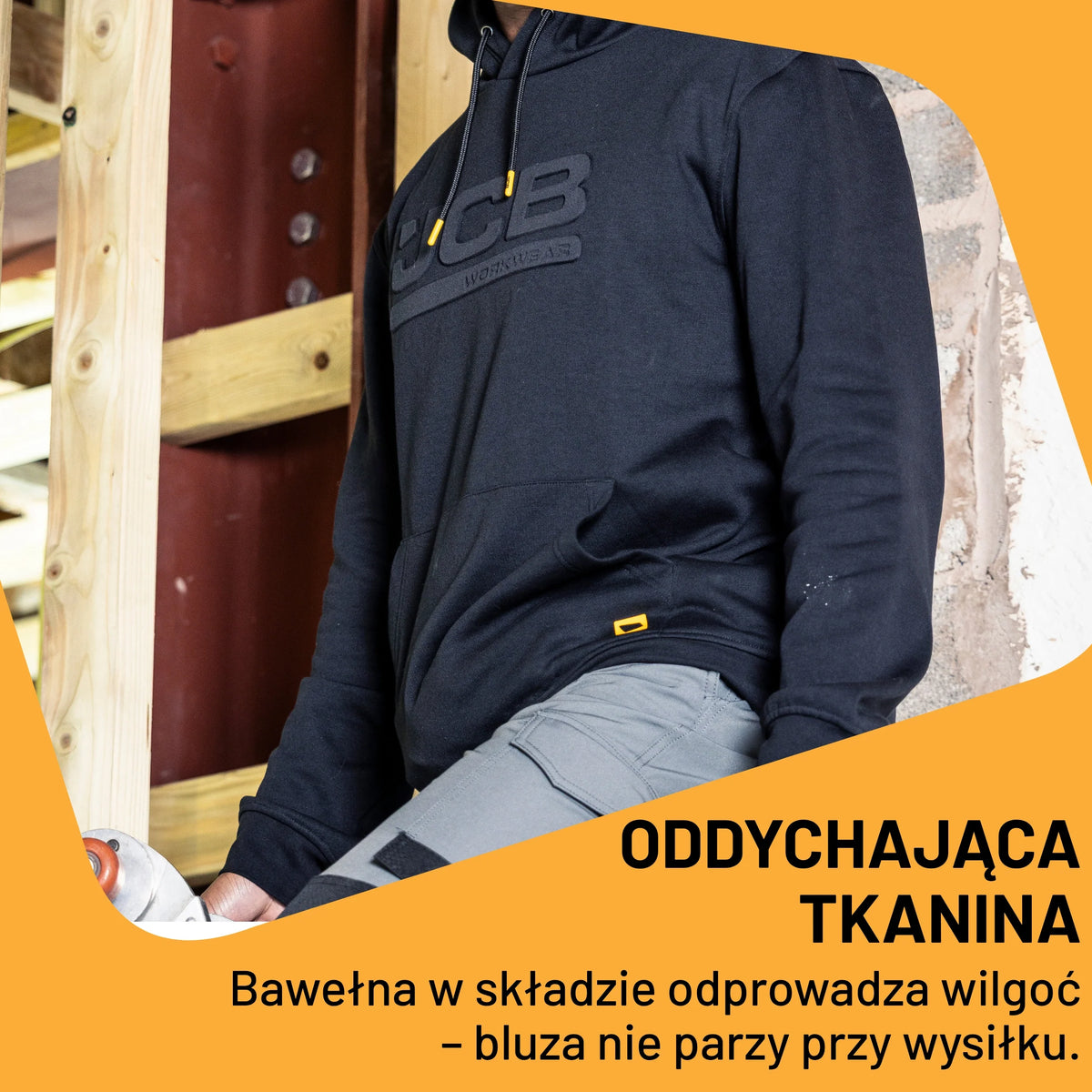 Mężczyzna w czarnej bluzie JCB z kapturem przy budowie, tekst Oddychająca tkanina
