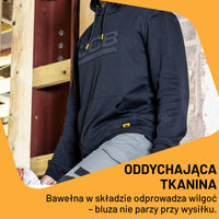 Mężczyzna w czarnej bluzie JCB z kapturem przy budowie, tekst Oddychająca tkanina