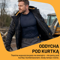 Mężczyzna w granatowej koszulce termoaktywnej JCB pod kurtką na budowie, tekst Oddycha pod kurtką