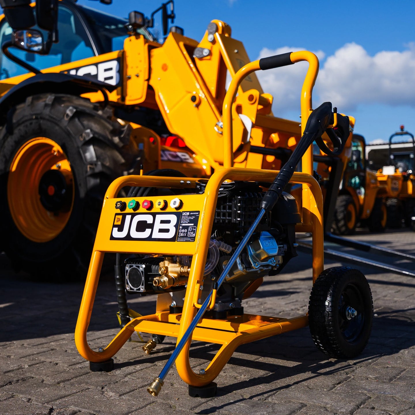 Myjka ciśnieniowa JCB PW7532P24 ujęcie z przodu z lancą opartą o ramę pompą annovi reverberi kołami terenowymi na placu z maszynami JCB