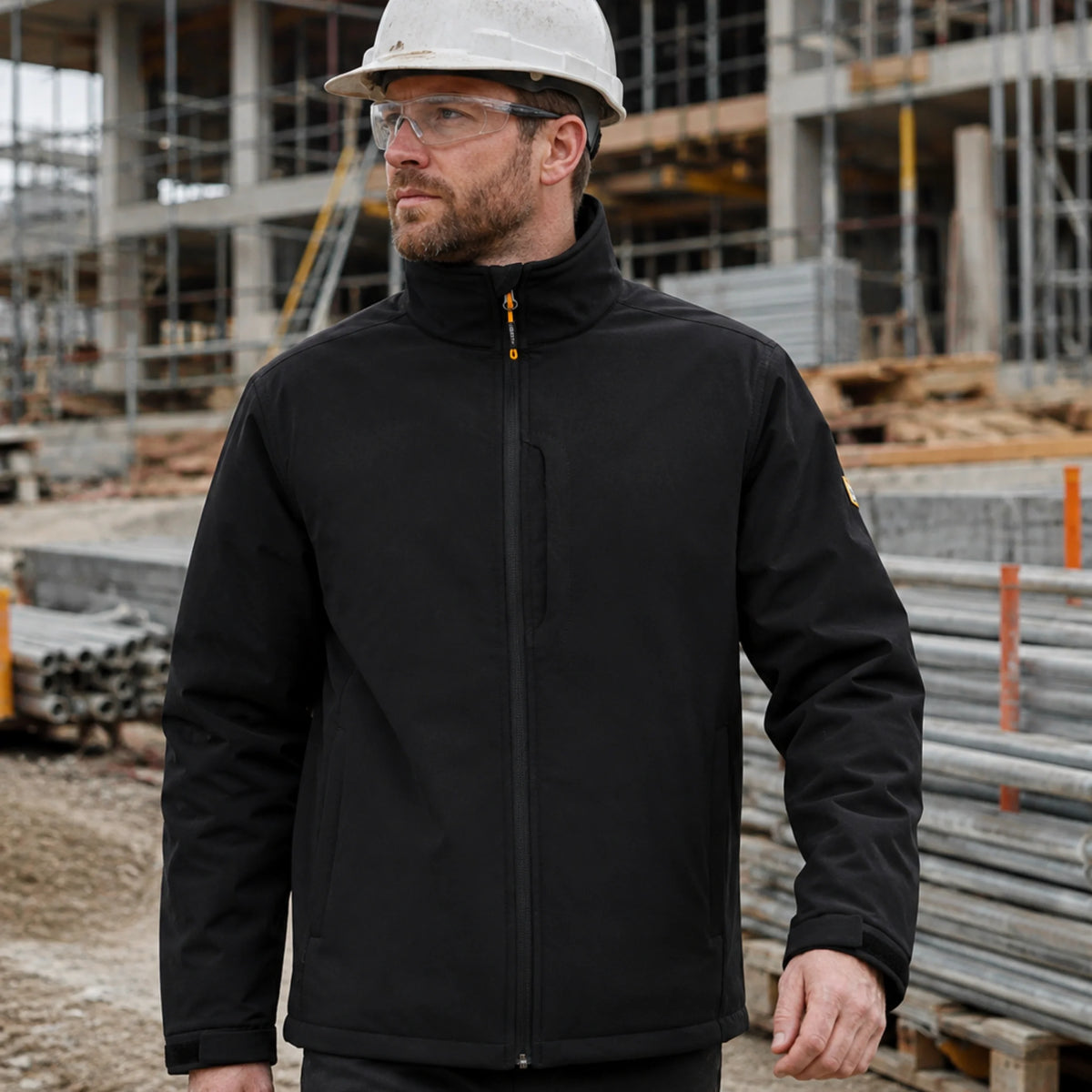 Mężczyzna w czarnej kurtce roboczej softshell JCB w kasku na placu budowy, ujęcie z przodu
