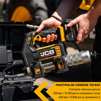 Smarownica akumulatorowa JCB 18V z zestawu JCB-PRO18V-SERVKIT-zestaw-1 trzymana w dłoni nad skrzynią narzędziową tekst maksymalne ciśnienie 700 bar